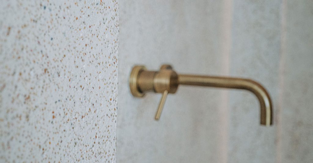 Close-up detail of microtopping in bathroom wall showing speckled texture finish with mounted brass faucet fixture